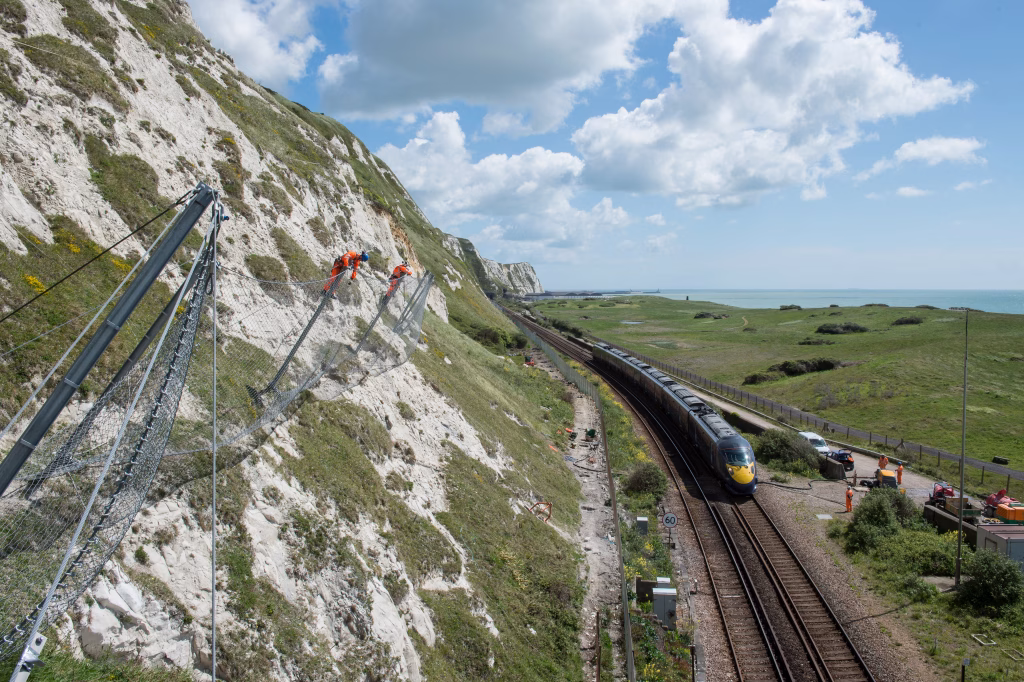 Workers installing a catch fence above a railway line.