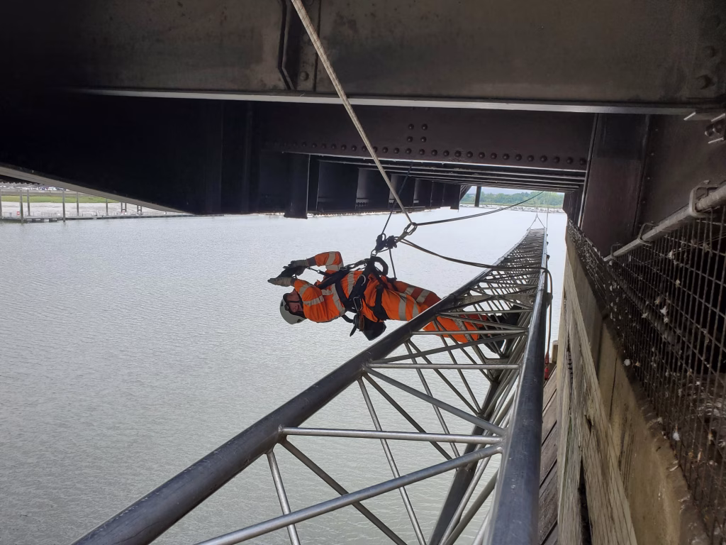 Worker carrying out an inspection horizontally secured by ropes on a beam.